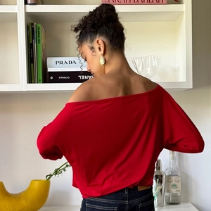 Red off-shoulder long-sleeve top shown from the back in a stylish lifestyle setting