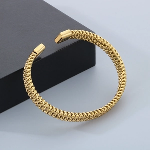 Close-up of golden stainless steel C-shaped braided texture bangle on a gift box