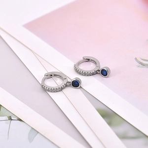 Detail of silver drop earrings featuring white zircon pavé and round blue stones
