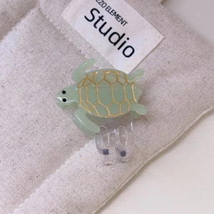 Close-up of green sea turtle hair claw clip with golden shell pattern on canvas bag