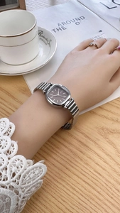 Detail of a square silver quartz watch with a brown dial worn on a woman's wrist