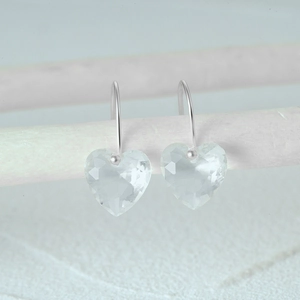 Macro shot of silver S925 heart earrings with faceted crystal hanging on a white stand
