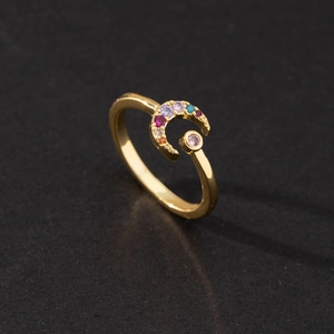 Macro shot of gold crescent moon ring inlaid with colorful rainbow zircons on black background