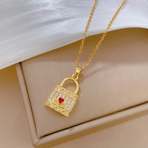 Gold heart lock necklace with white crystals and a red ruby center on silk background