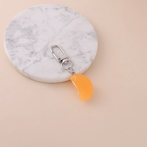 Close-up of a realistic orange segment keychain on a white marble coaster background