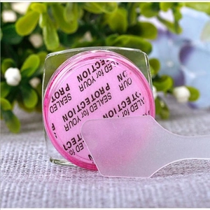 Detail of pink face cream jar with protective seal and a translucent scoop tool
