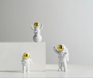 Three white astronaut figurines with gold visors displayed on a minimalist white stand