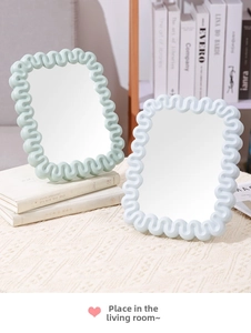 Detail of wavy-edged makeup mirrors in pastel blue and green on a woven tablecloth