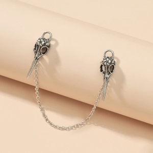Gothic silver bird skull chain brooch with vintage texture on a beige background