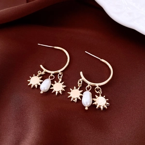 Detailed shot of golden sun pendants and baroque pearl on C-shaped stud earrings