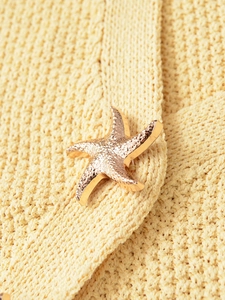 Detail of a gold starfish button on a light yellow knit fabric texture