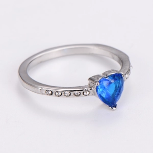 Detailed close-up of a silver heart ring featuring a blue gemstone and white zircon accents