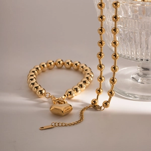 Detail shot of golden beaded necklace and bracelet set with 3D heart charms on glass