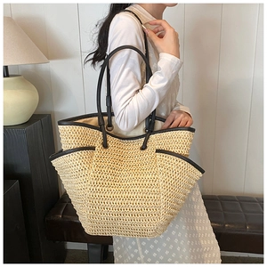 Large straw tote bag with black leather shoulder straps shown on a model for beach style