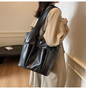 Side view of a black multi-pocket PU leather tote bag worn with a beige trench coat