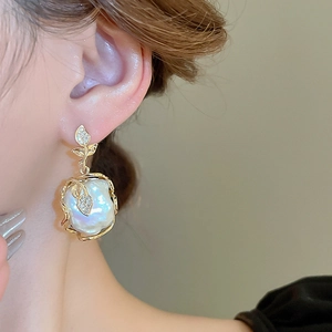 Gros plan d'une femme portant des boucles d'oreilles fleur en perle baroque dorée