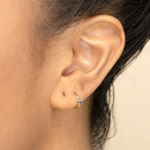 Detalle de un pendiente de aro de oro de 18k con circón azul en una oreja femenina