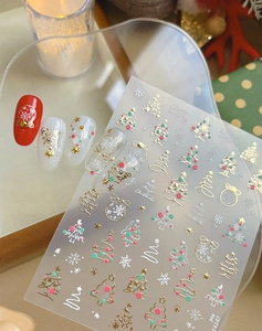 Detail of Christmas nail stickers with gold trees and snowflakes on manicured nails