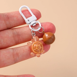 Detail of orange resin turtle keychain with brown acorn charm and white metal clip