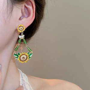 Macro detail of sunflower earrings with yellow enamel, green beads and butterfly charms