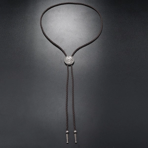 Detail of vintage silver bolo tie buckle with dark brown woven leather cord and metal tips