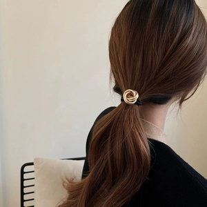 Elegant gold metal twist hair tie with black elastic band shown on a ponytail