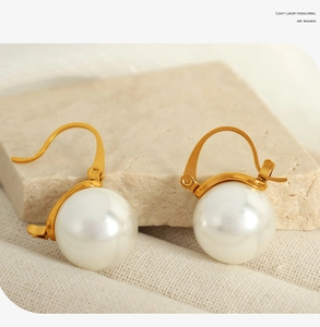 Détail de boucles d'oreilles dorées avec perles blanches rondes sur pierre texturée