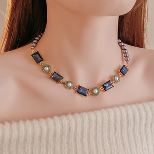 Detail of vintage necklace with blue square gem, white pearls and gold rings on model neck