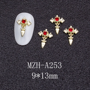 Macro detail of gold winged cross nail charms with red rhinestones on white nail tips
