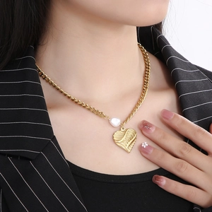 Close-up of golden heart pendant necklace with textured wing detail and white pearl bead
