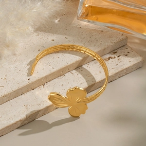 Bracelet jonc ouvert fleur plaqué or 18 carats élégant sur surface en travertin