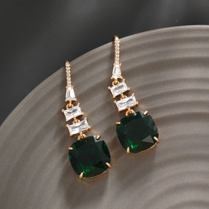 Macro shot of long drop earrings with emerald green stones and clear cubic zirconia on a gray tray