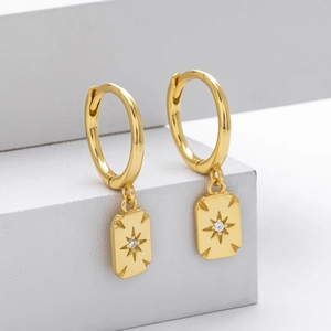 Detailed macro view of gold-plated hoop earrings with an engraved star-burst zircon pendant