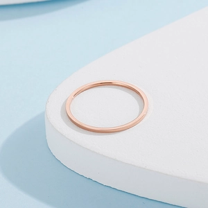 Minimalist rose gold stainless steel ring on white geometric stand with blue background