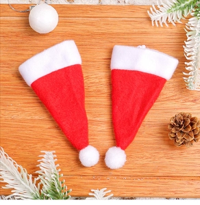 Pair of mini red and white plush Christmas hats on wood with festive pine cones