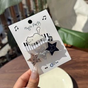 Close-up of music-themed hair clip set featuring cat, piano and note motifs on card