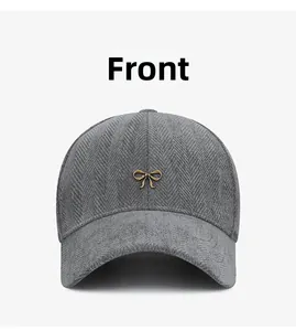 Détail du tissu à chevrons gris foncé et du nœud papillon en métal doré sur la casquette