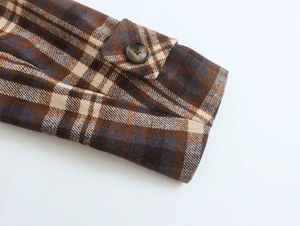 Detail of brown plaid wool jacket cuff with decorative button strap and woven texture