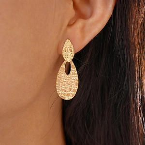 Close-up of gold geometric teardrop earrings with textured metal surface on model
