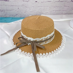 Macro view of woven straw hat featuring white lace trim and a brown checkered ribbon bow