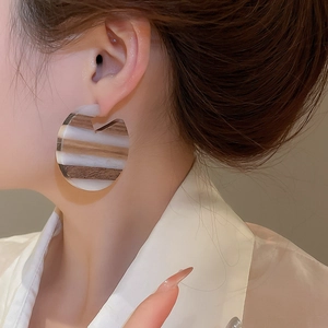 Close-up of geometric C-shaped brown wood grain and white resin earrings worn by a model