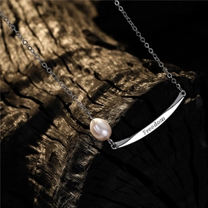 Minimalist pearl necklace with silver Freedom engraved pendant on a rustic wood background