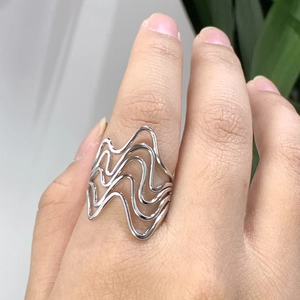 Nahaufnahme eines mehrlagigen wellenförmigen Silberrings mit hohlem Design am Finger