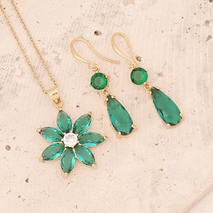 Detailed view of emerald green gemstone flower necklace and matching earring set on stone