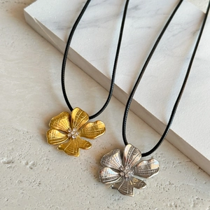 Detail of 18k gold and silver flower pendants with crystals on black cord necklace