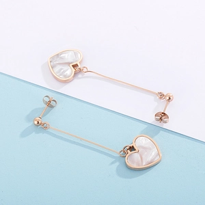 Detail view of rose gold heart earrings with white shell inlay on a blue and white background