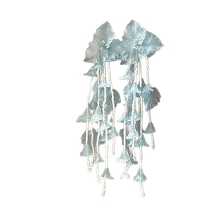 Boucles d'oreilles fleurs bleu clair avec pompons perlés blancs sur fond blanc épuré