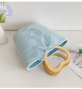Close-up of light blue woven handbag with heart wooden handle and tulle bow decoration