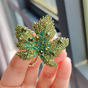 Detailed macro view of crystal maple leaf brooch with green gradient rhinestones
