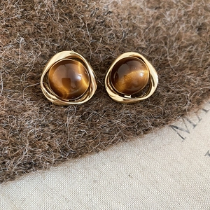Detailed close-up of geometric 18k gold plated tiger eye stone earrings on soft fabric